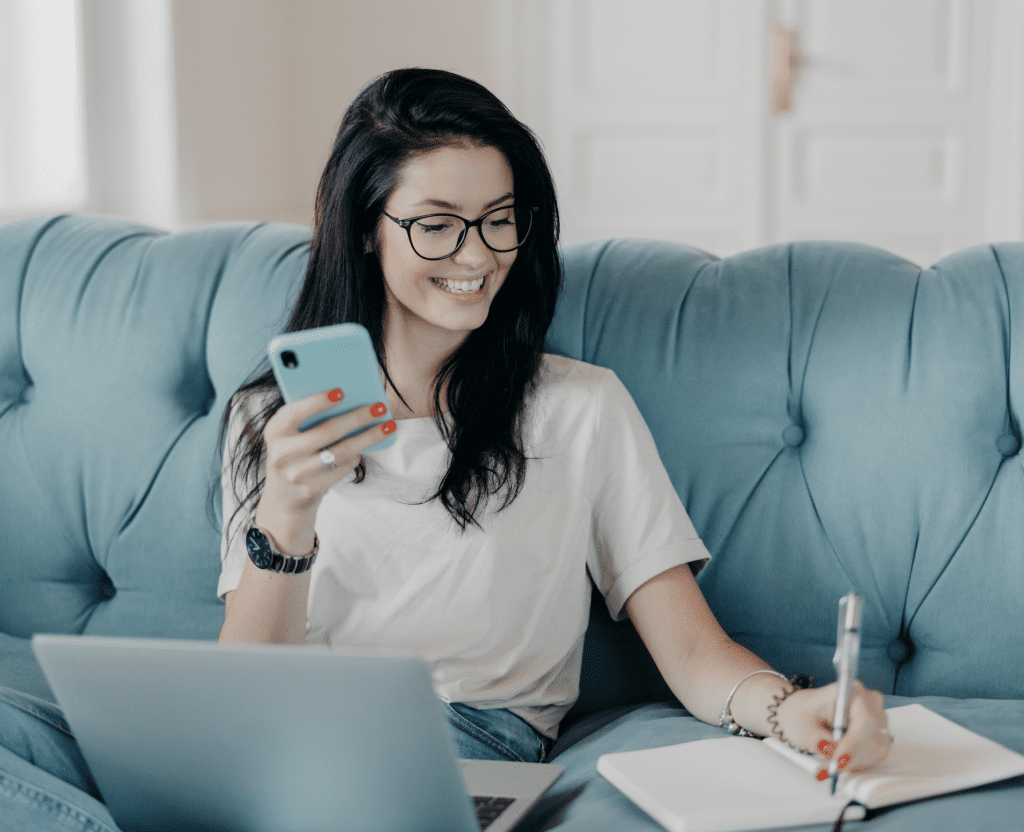 A woman sitting on a couch with a laptop and cell phone.